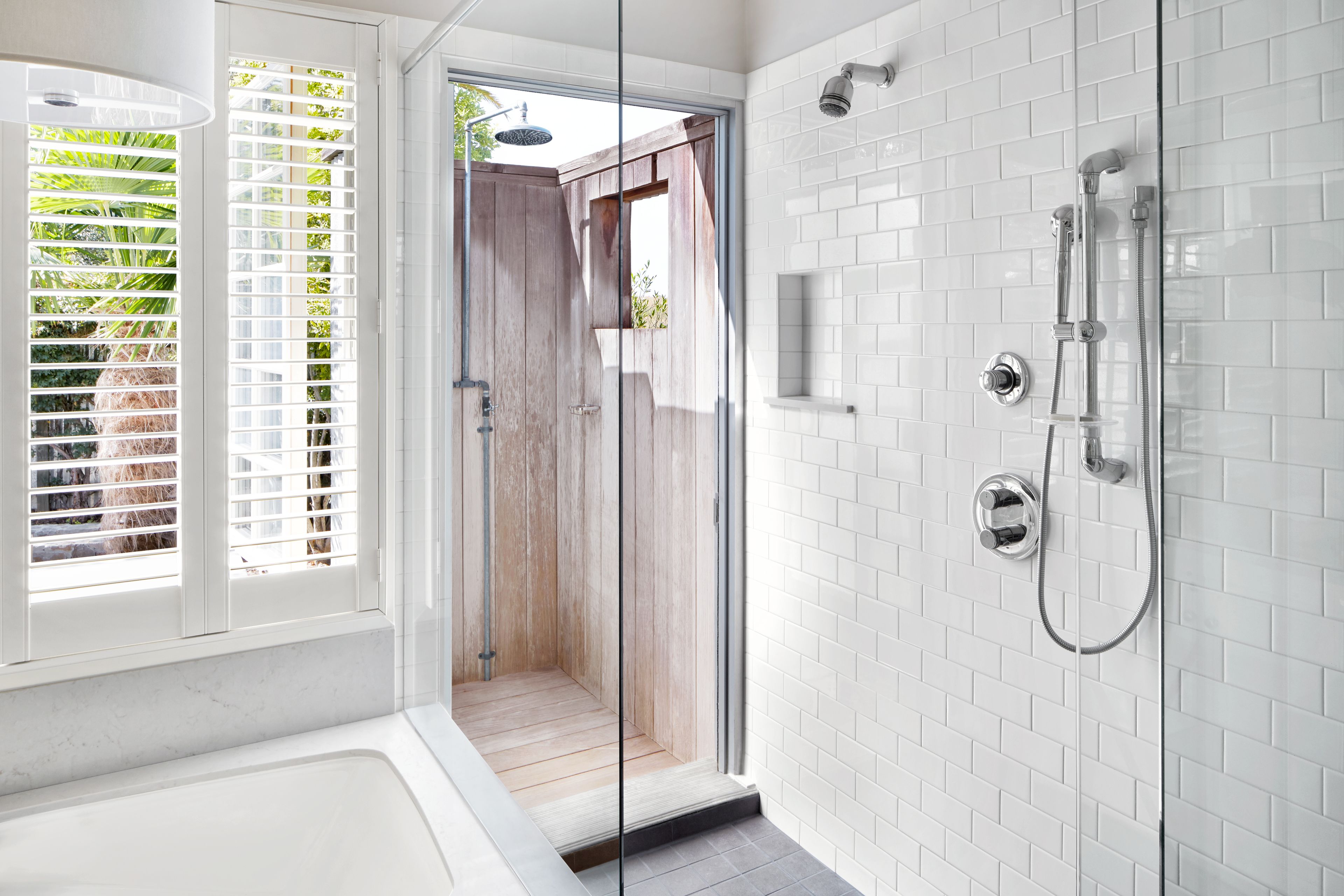 A modern bathroom with a glass-enclosed shower, white tiled walls, and a wooden door.