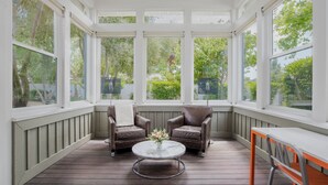 A sunroom with two leather chairs, a glass table, and a bench.