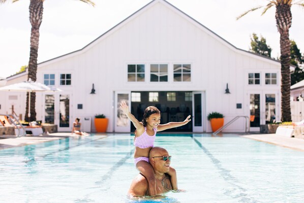 A swimming pool with a white building in the background, palm trees, and lounge chairs. - Carneros Resort and Spa (Napa)