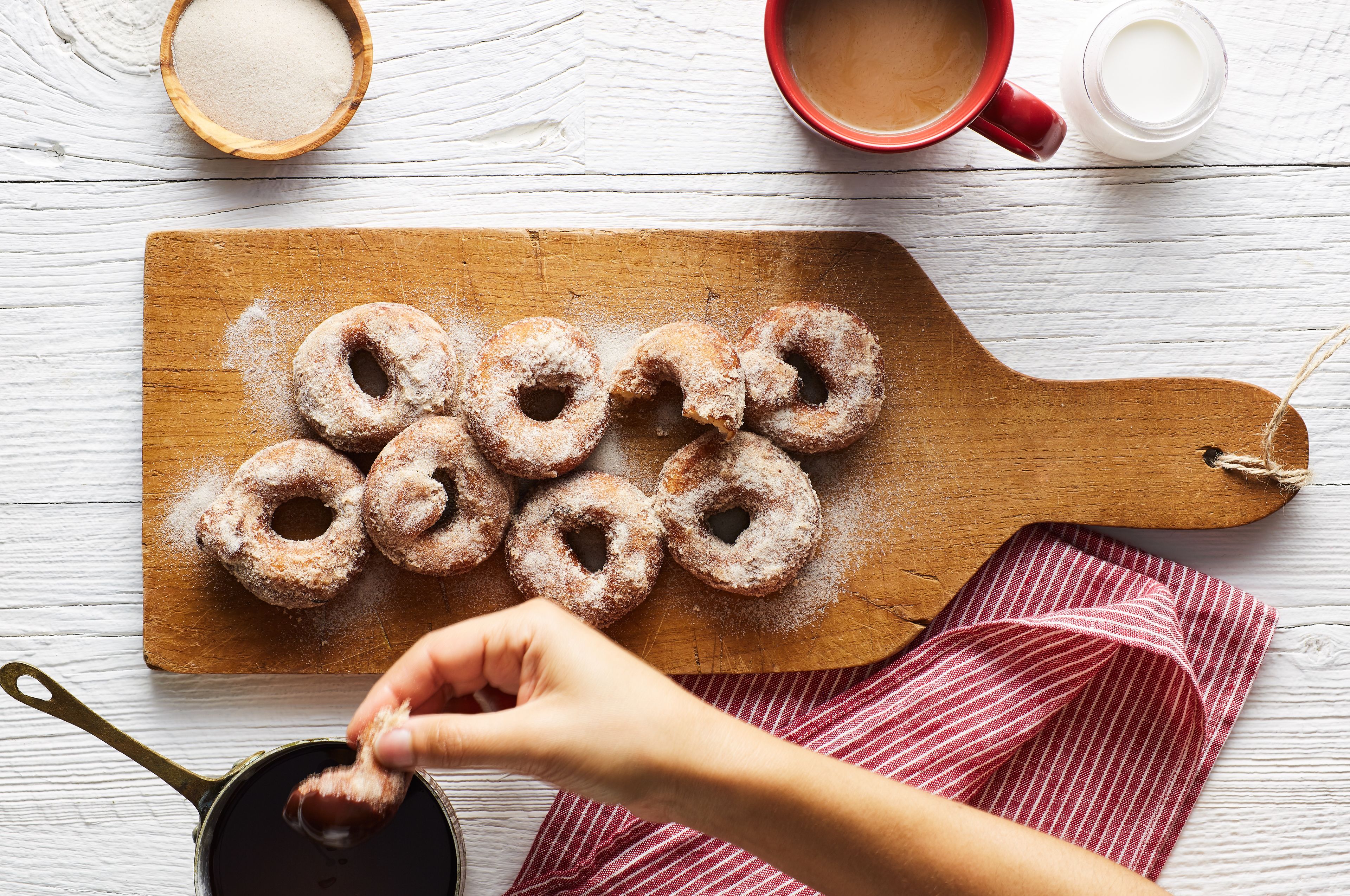 Una tabla de madera con seis rosquillas espolvoreadas con azúcar y una mano escogiendo una.
