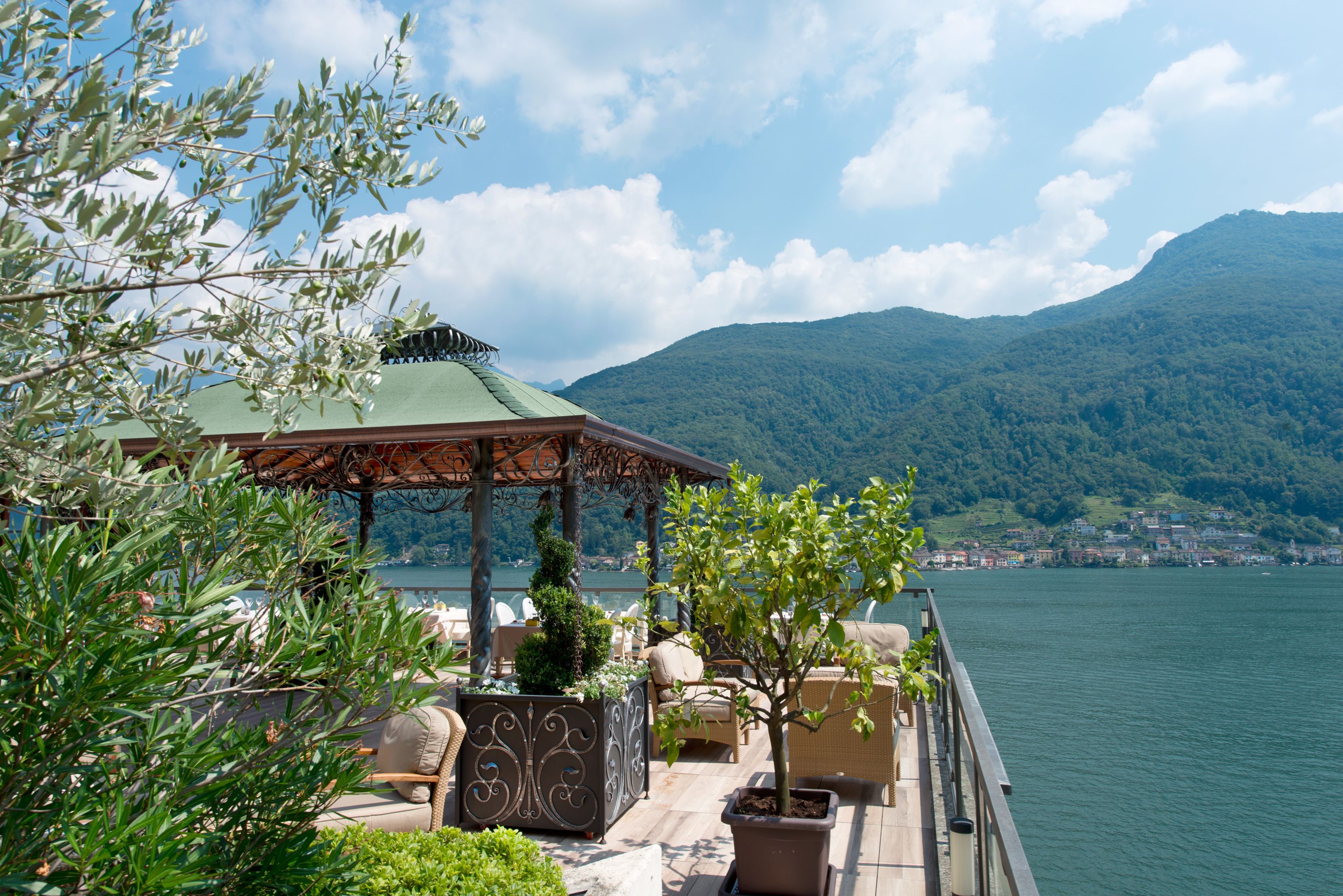 A terrace with outdoor seating, a pergola, and a view of a lake and mountains.