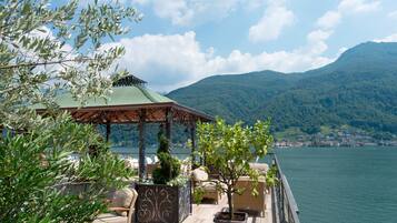 A terrace with outdoor seating, a pergola, and a view of a lake and mountains.