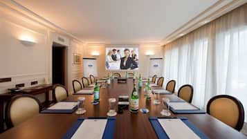 Ein Konferenzraum mit langem Tisch, Stühlen, einer Projektionsleinwand und abgefülltem Wasser.