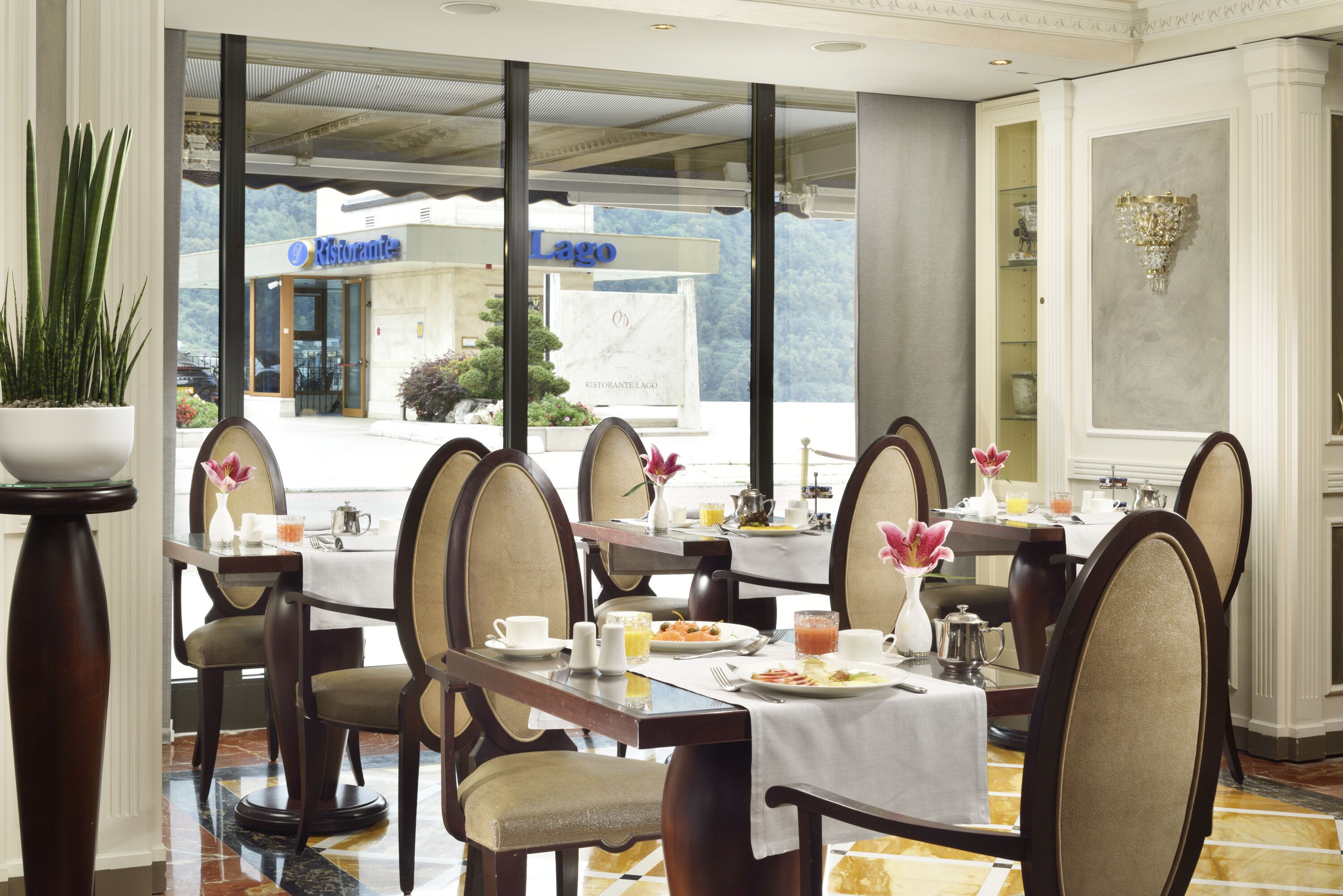 Comedor con mesas dispuestas para el desayuno, sillas con asientos acolchados y vistas al restaurante 'Lago'.