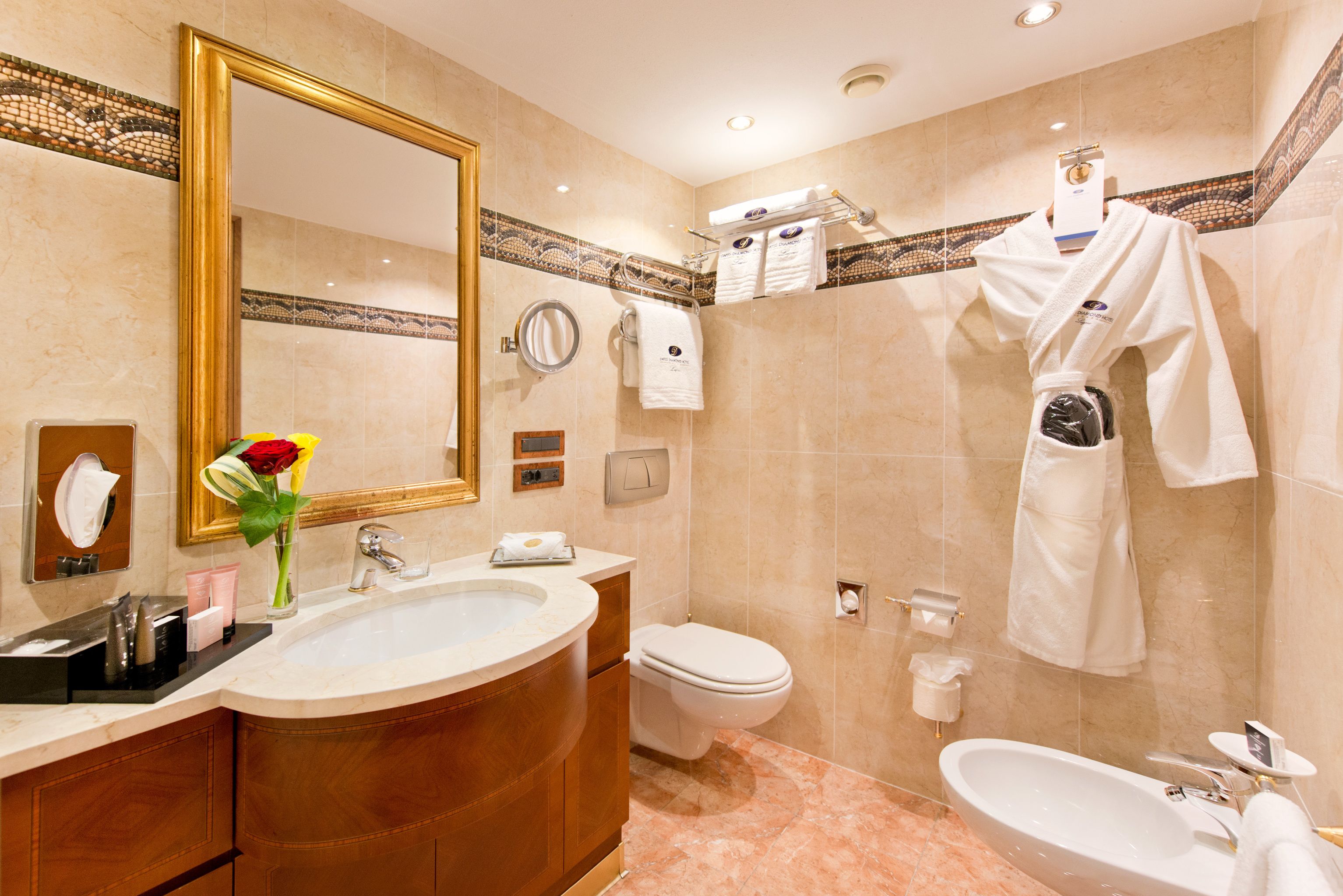 A bathroom with a large mirror, a sink, a toilet, and a bidet. There are towels and toiletries on the counter.