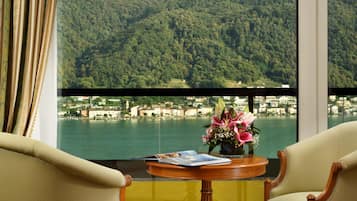 A room with a view of a lake and mountains, a table with a book and flowers, and two chairs.