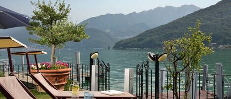 Una terraza junto al lago con sillones, una mesa con una bebida y una planta en maceta.