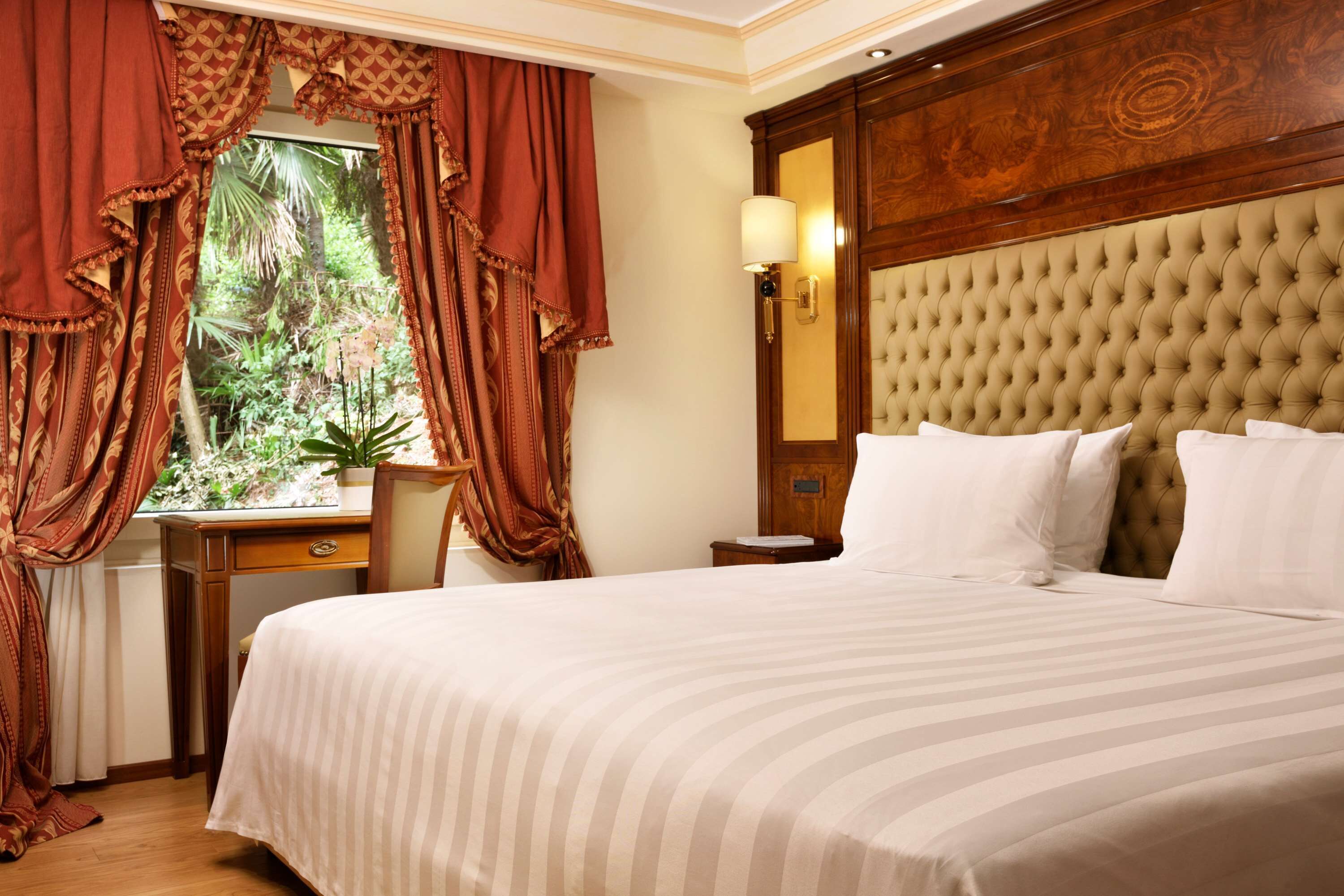 A hotel room with a large bed, a desk, and a window with curtains.