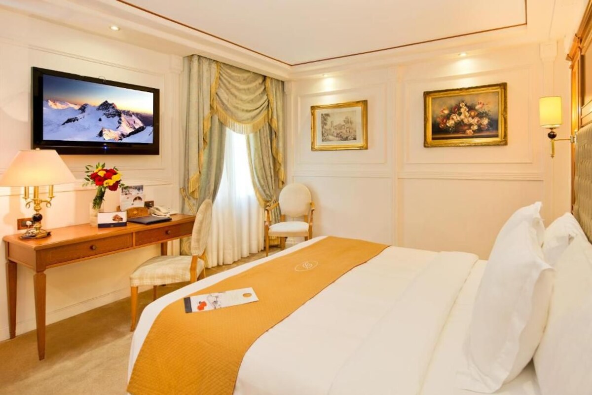 Habitación de hotel con cama, escritorio, silla, televisor y obras de arte en las paredes.