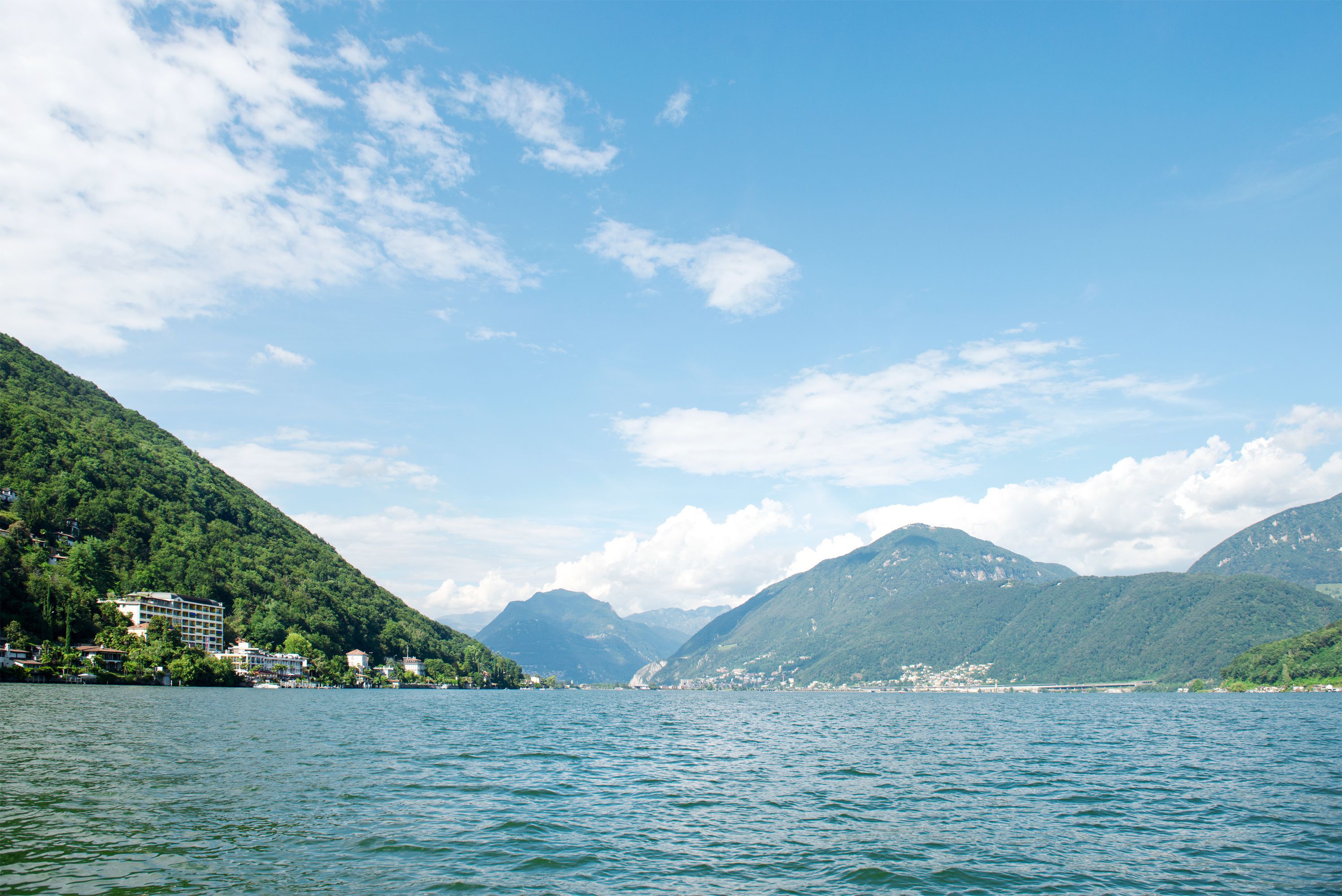 A lake with mountains in the background and buildings along the shore.