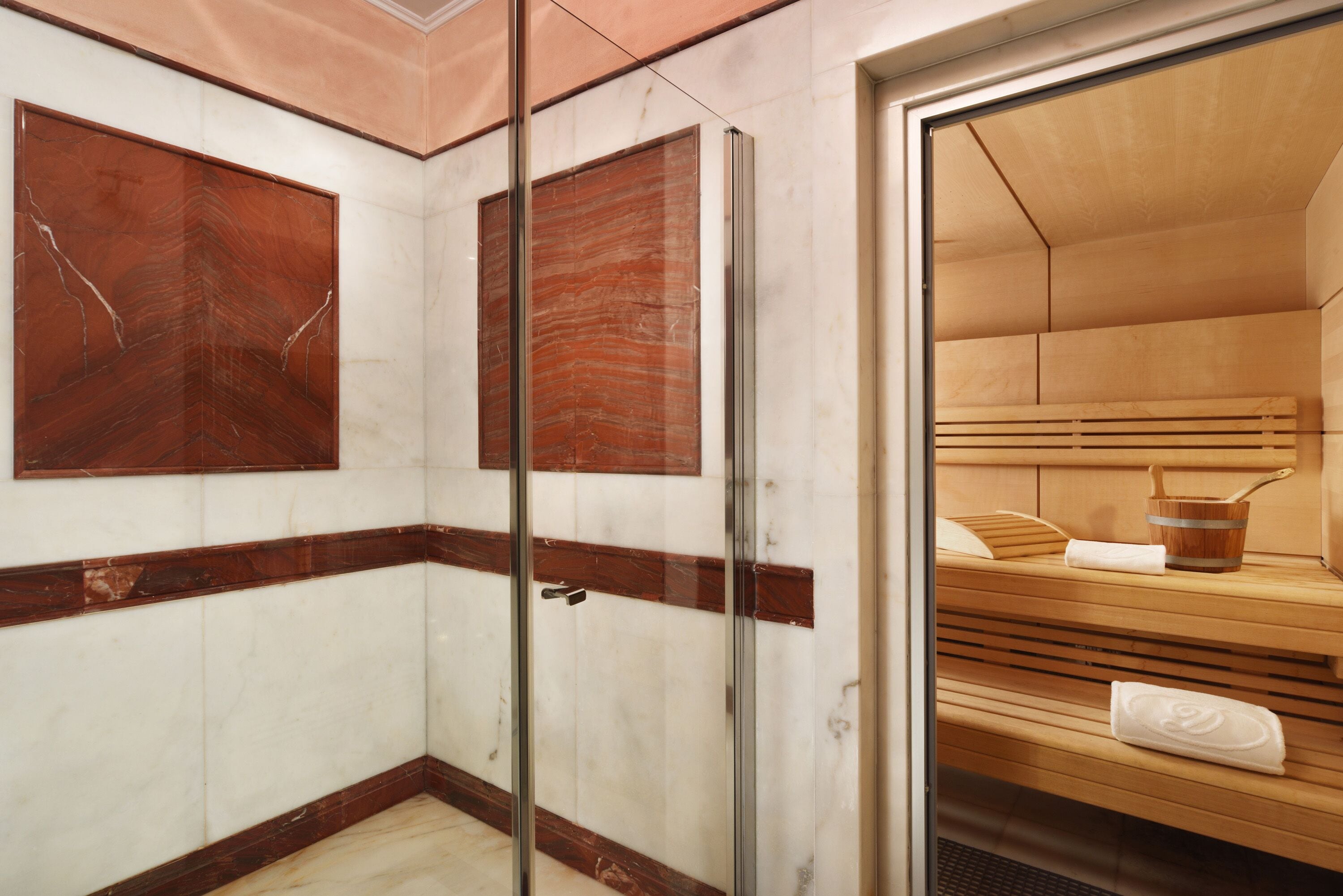 A modern bathroom with marble walls, a glass shower enclosure, and a wooden sauna bench.