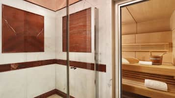 A modern bathroom with marble walls, a glass shower enclosure, and a wooden sauna bench.