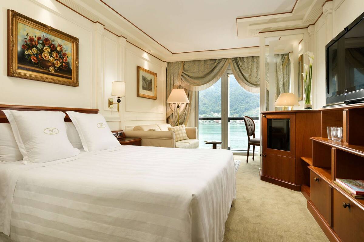 Quarto de hotel com uma cama grande, um sofá, uma TV e vista para a água.