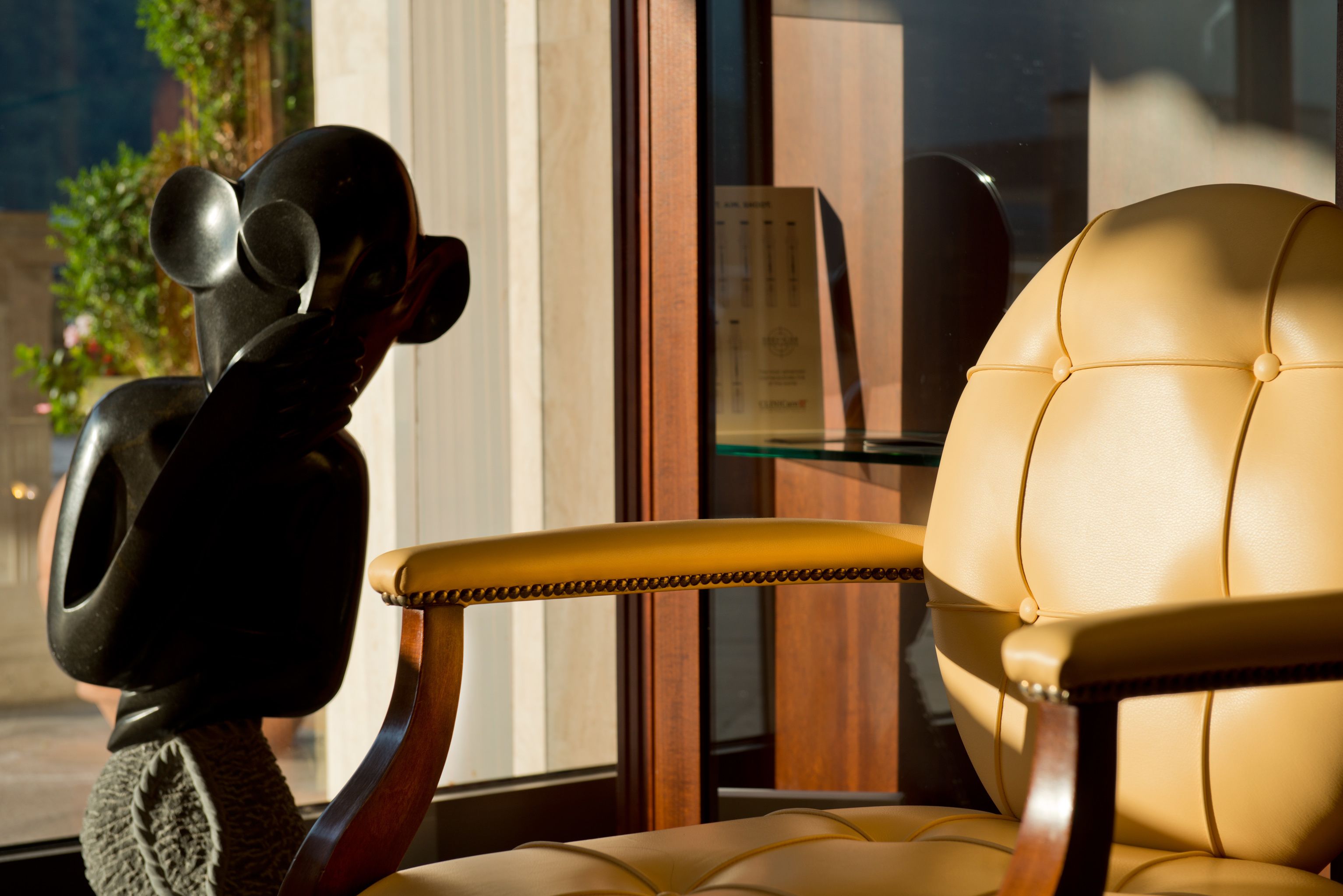A chair with a high back and cushioned seat, positioned near a window with a view of greenery outside.