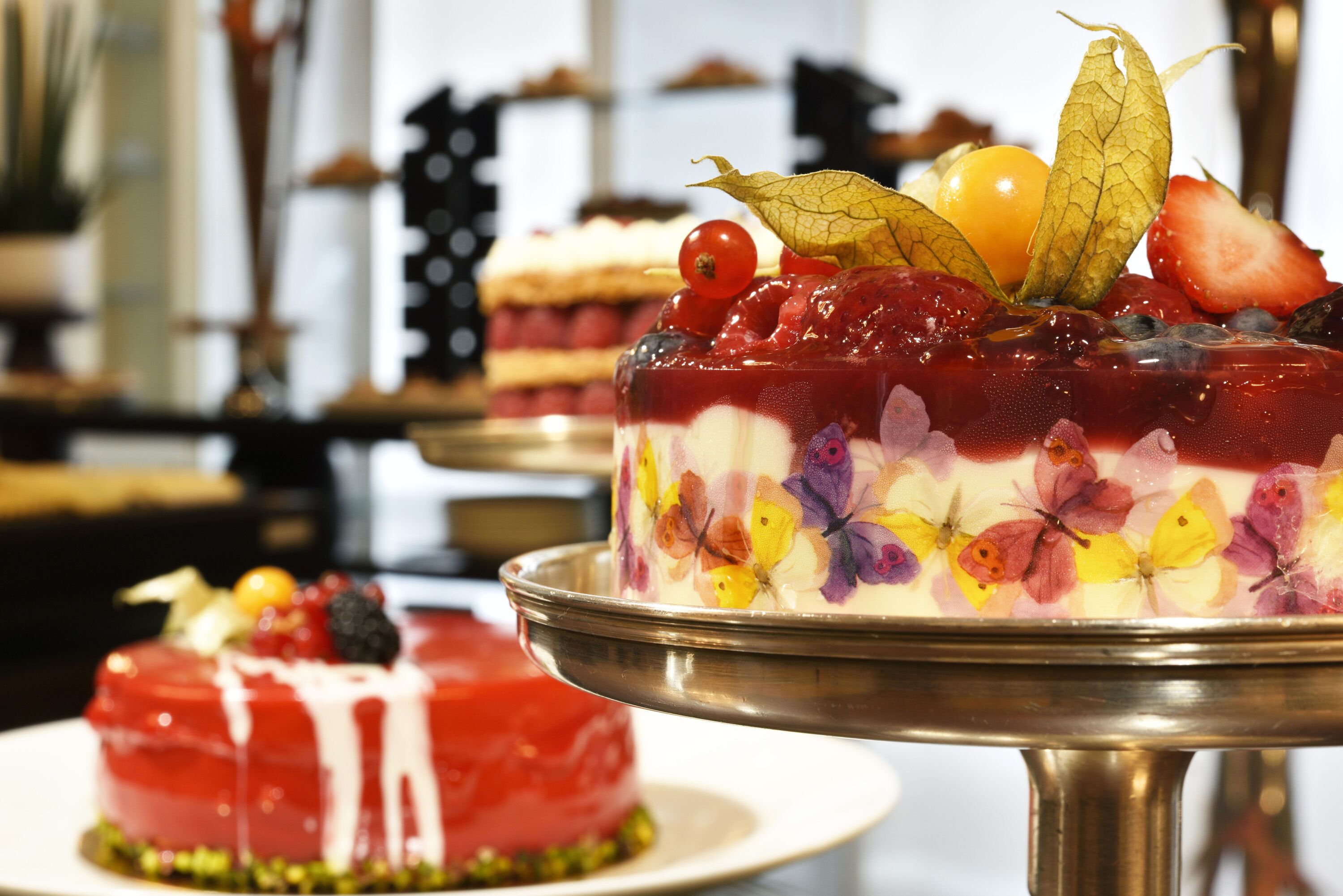 A dessert with layers of fruit and cream, garnished with berries and leaves, on a metal stand.