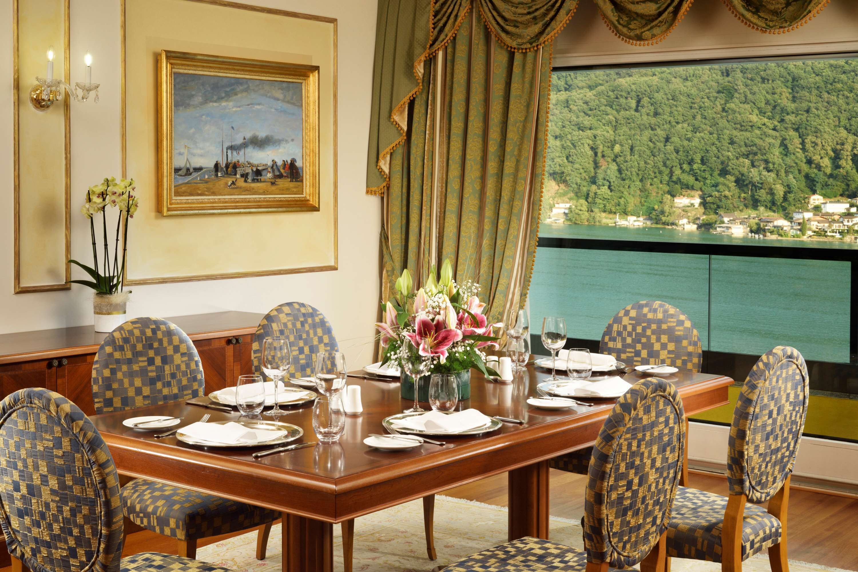 Una sala da pranzo con un tavolo in legno apparecchiato per sei persone, sedie decorate, un vaso con fiori e un quadro appeso alla parete.