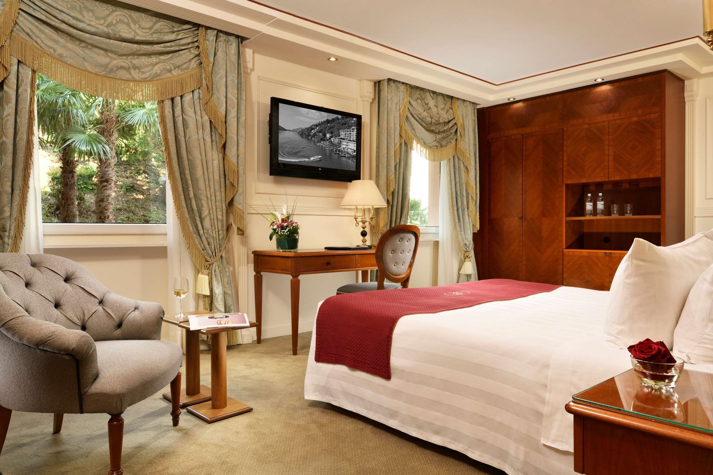 Een hotelkamer met een bed, een stoel, een bureau, een televisie en uitzicht op palmbomen.