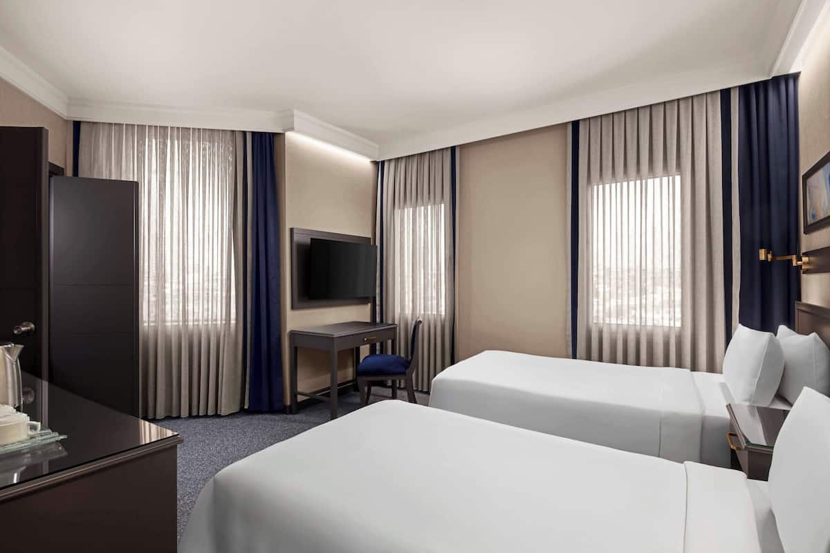 Ein Hotelzimmer mit zwei Betten, einem Schreibtisch, einem Fernseher und Vorhängen.
