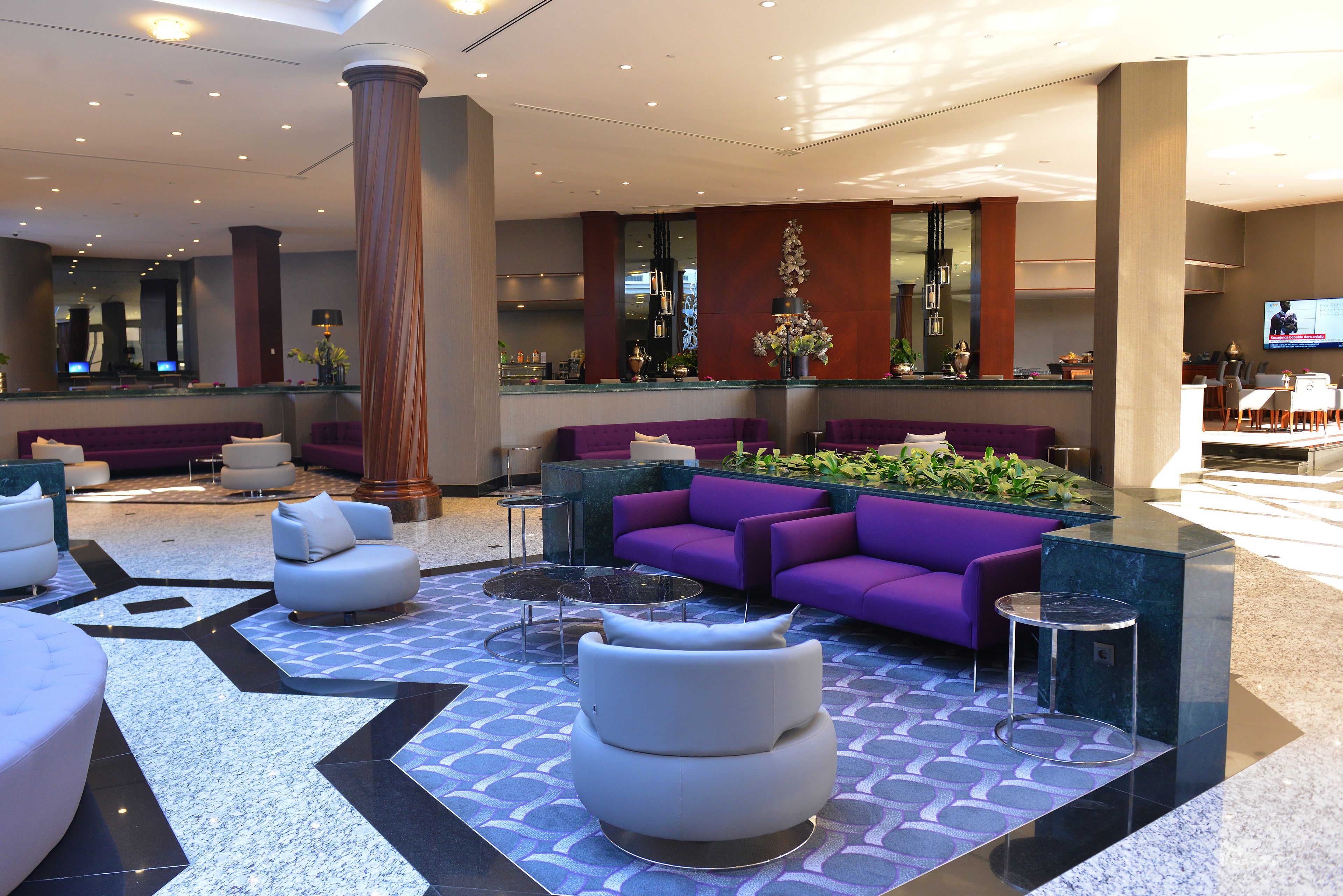 Un hall d’entrée moderne avec des canapés violets, des fauteuils blancs et un sol à motifs.