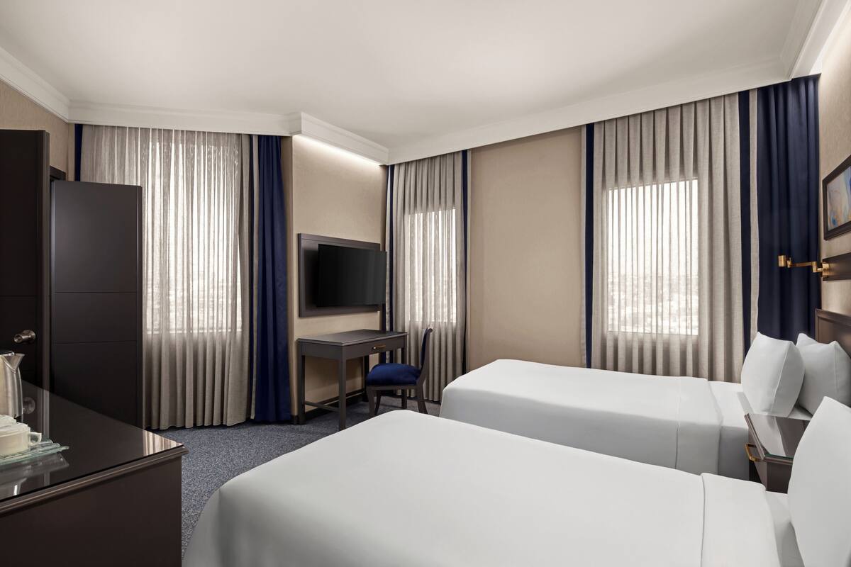 A hotel room with two beds, a desk, a TV, and a minibar.