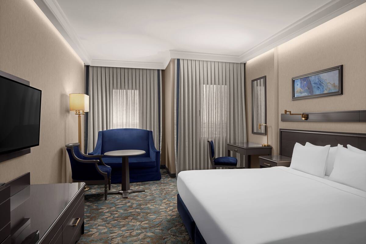 A hotel room with a large bed, a desk, a chair, a TV, and curtains.