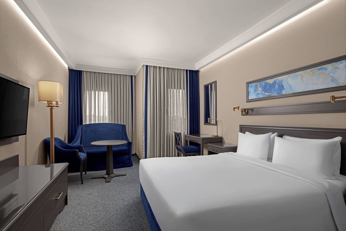A hotel room with a bed, a desk, a chair, a TV, and a lamp.