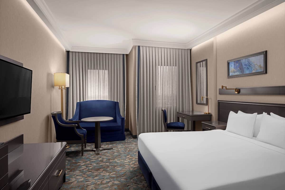 Ein Hotelzimmer mit Bett, Schreibtisch, Stuhl, Fernseher und Lampe.