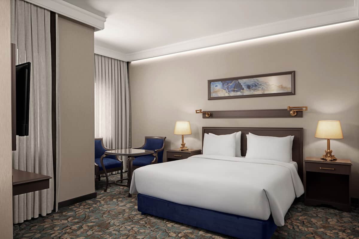 A hotel room with a large bed, two bedside tables with lamps, a chair, a desk, and a television.