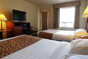 Two single beds with striped and patterned bedspreads, a flat-screen TV, and a desk with a lamp.