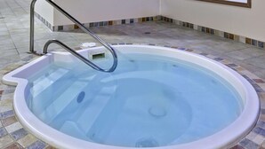 Un jacuzzi con escalera metálica, rodeado de piso de baldosas.