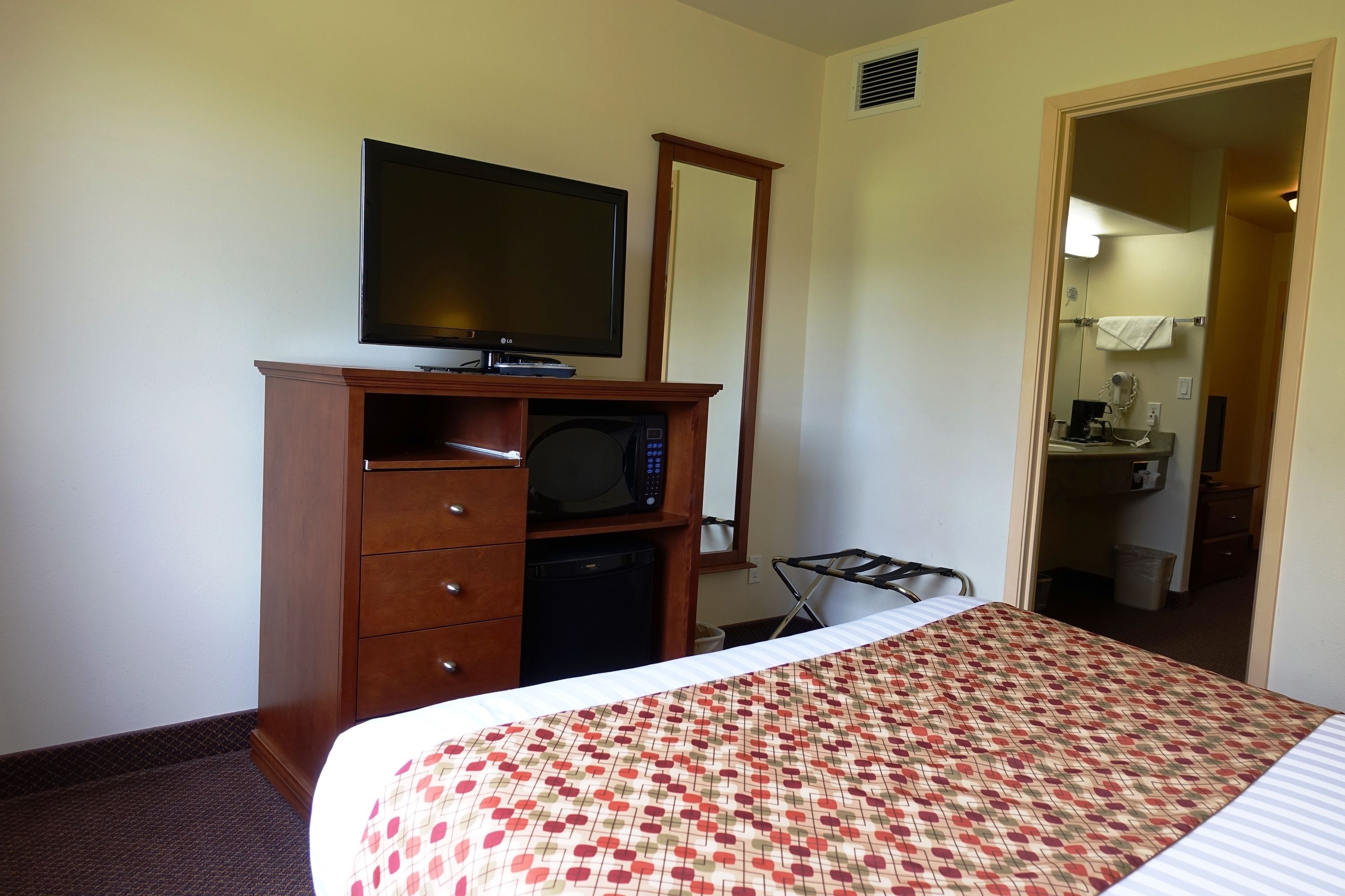 A hotel room with a bed, a dresser with a television, a microwave, and a small desk area.