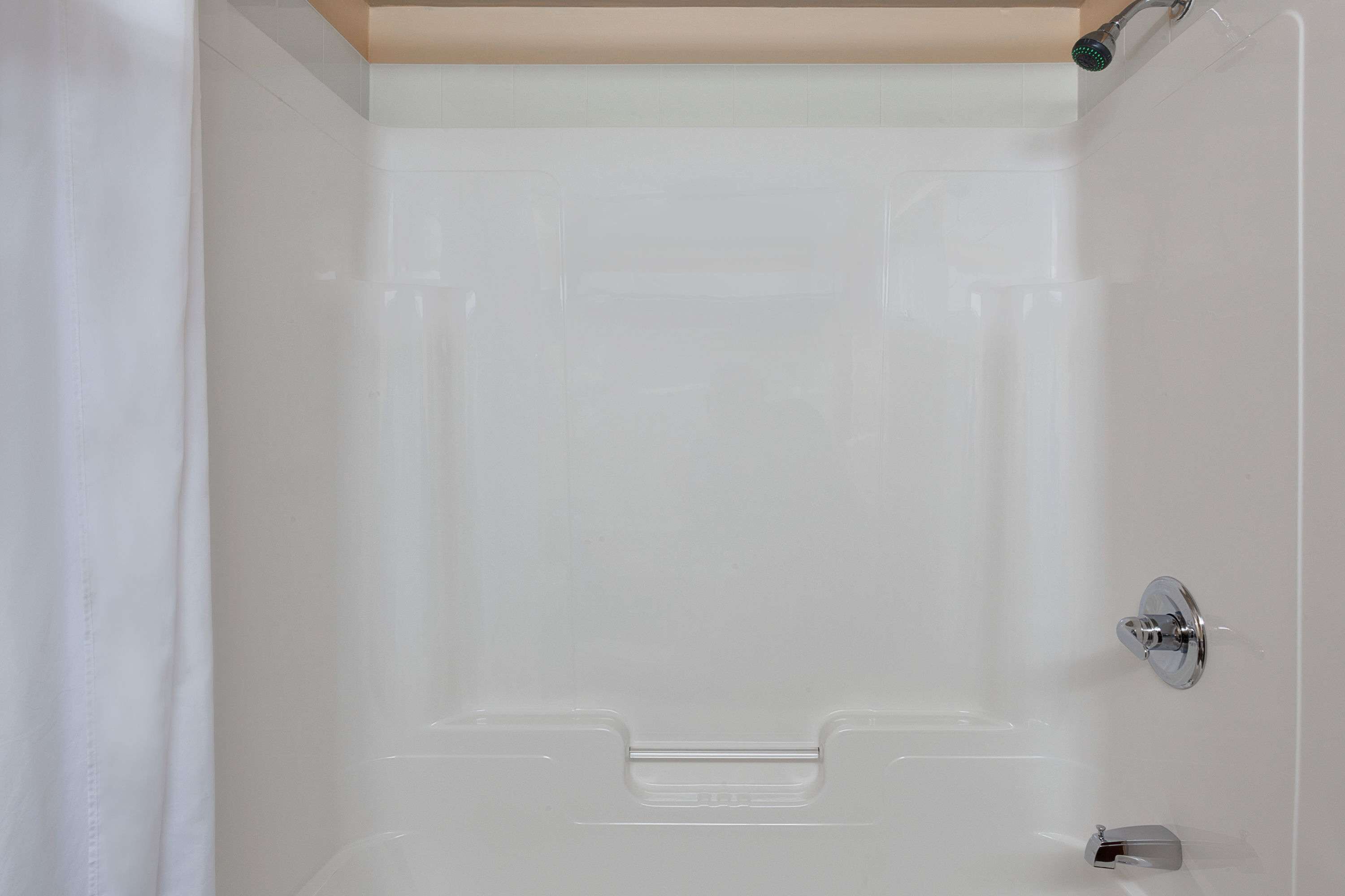 A bathroom with a white bathtub, a shower area, and a door with a silver handle.