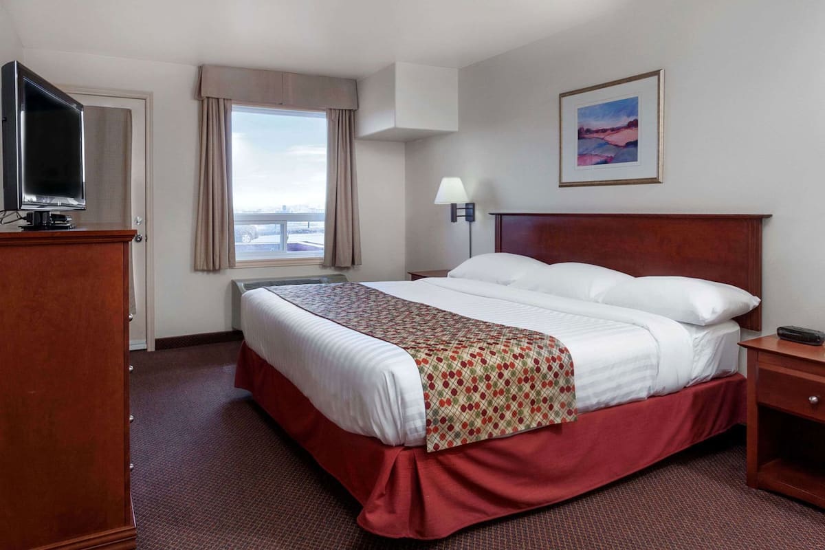 A hotel room with a bed, a TV, a desk, a lamp, and a window with a view.