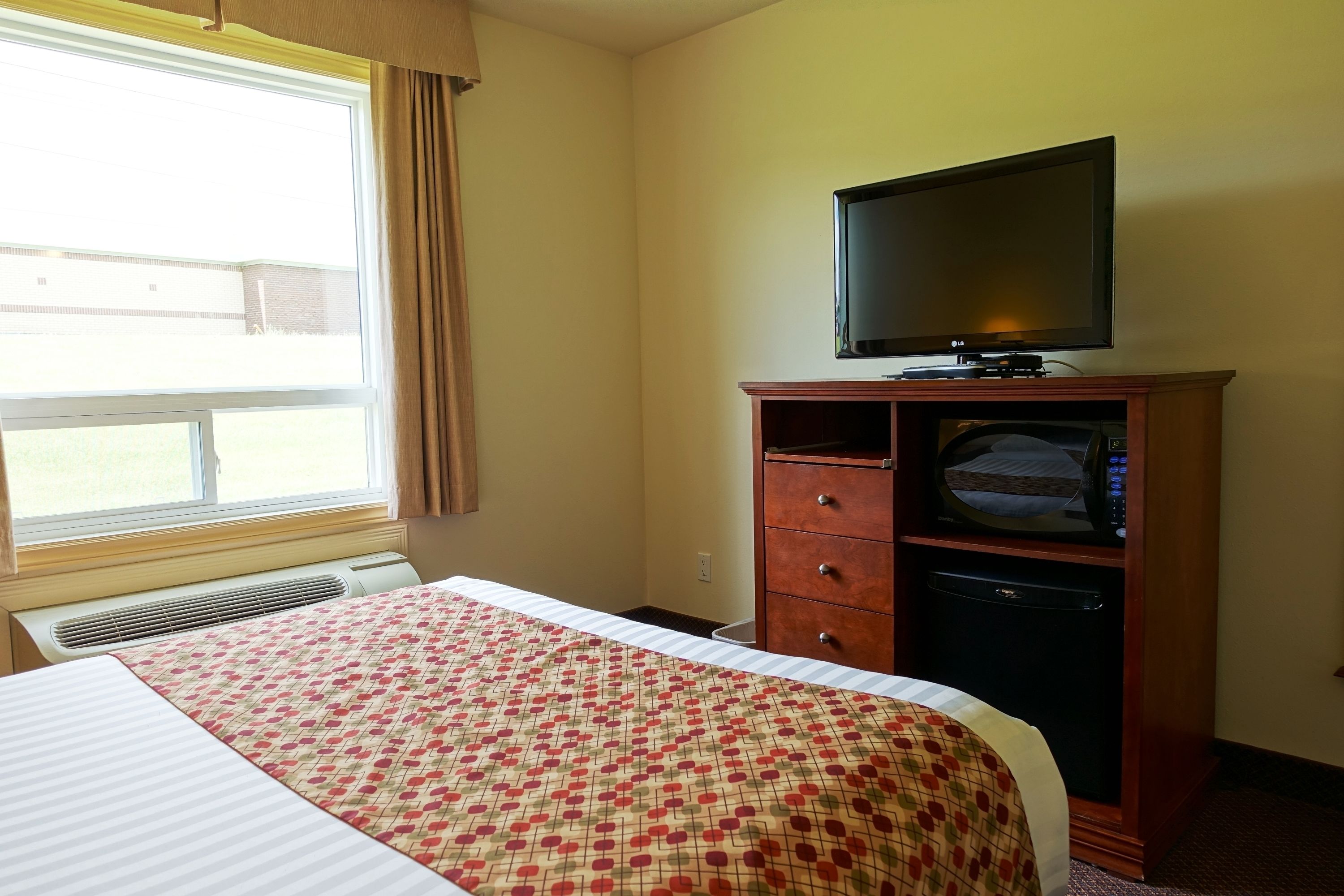 Quarto de hotel com uma cama, televisão sobre um armário de madeira e janela com cortinas.