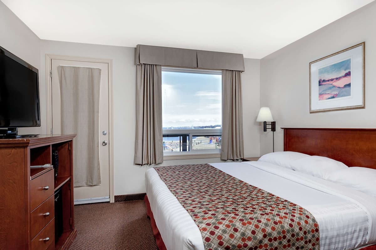 A hotel room with a bed, a TV, a desk, a window with curtains, a lamp, and a painting on the wall.
