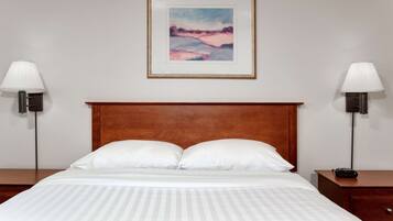 Una cama bien hecha con ropa de cama blanca, un cabecero de madera y un cuadro enmarcado encima.
