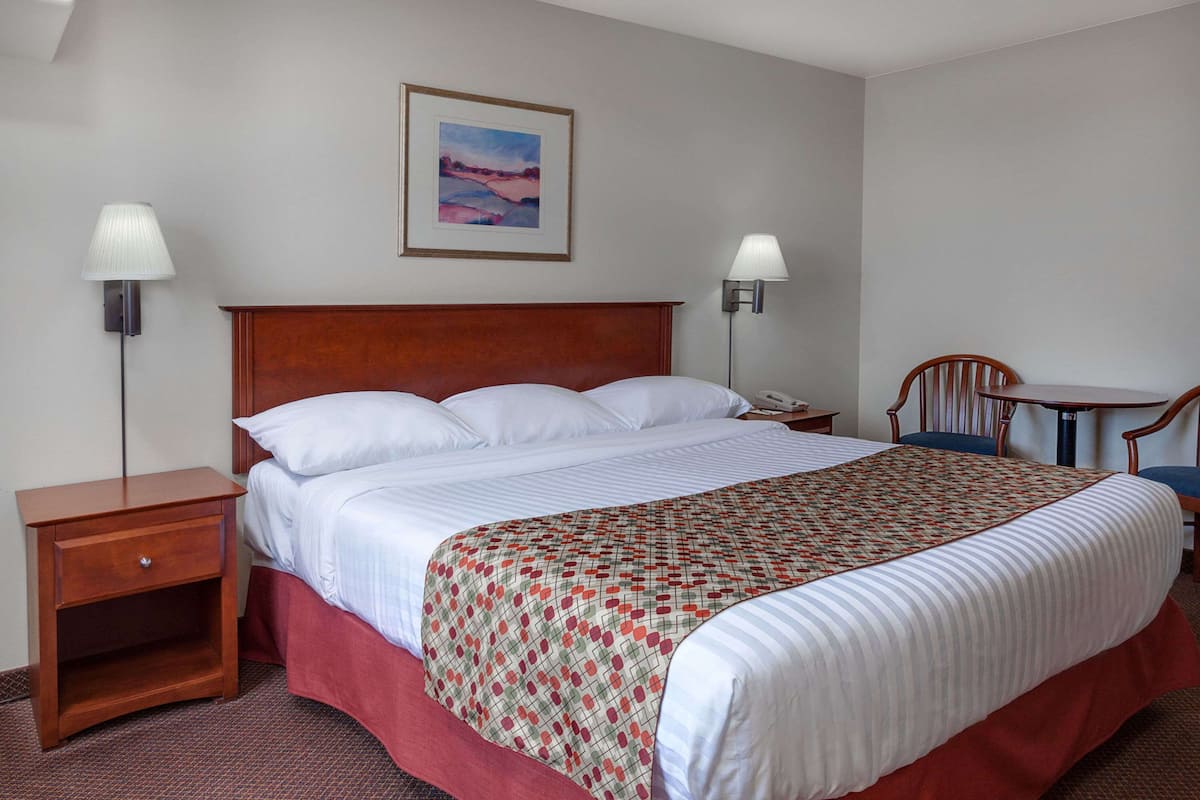 A hotel room with a large bed, two bedside tables, a chair, a small table, and a painting on the wall.