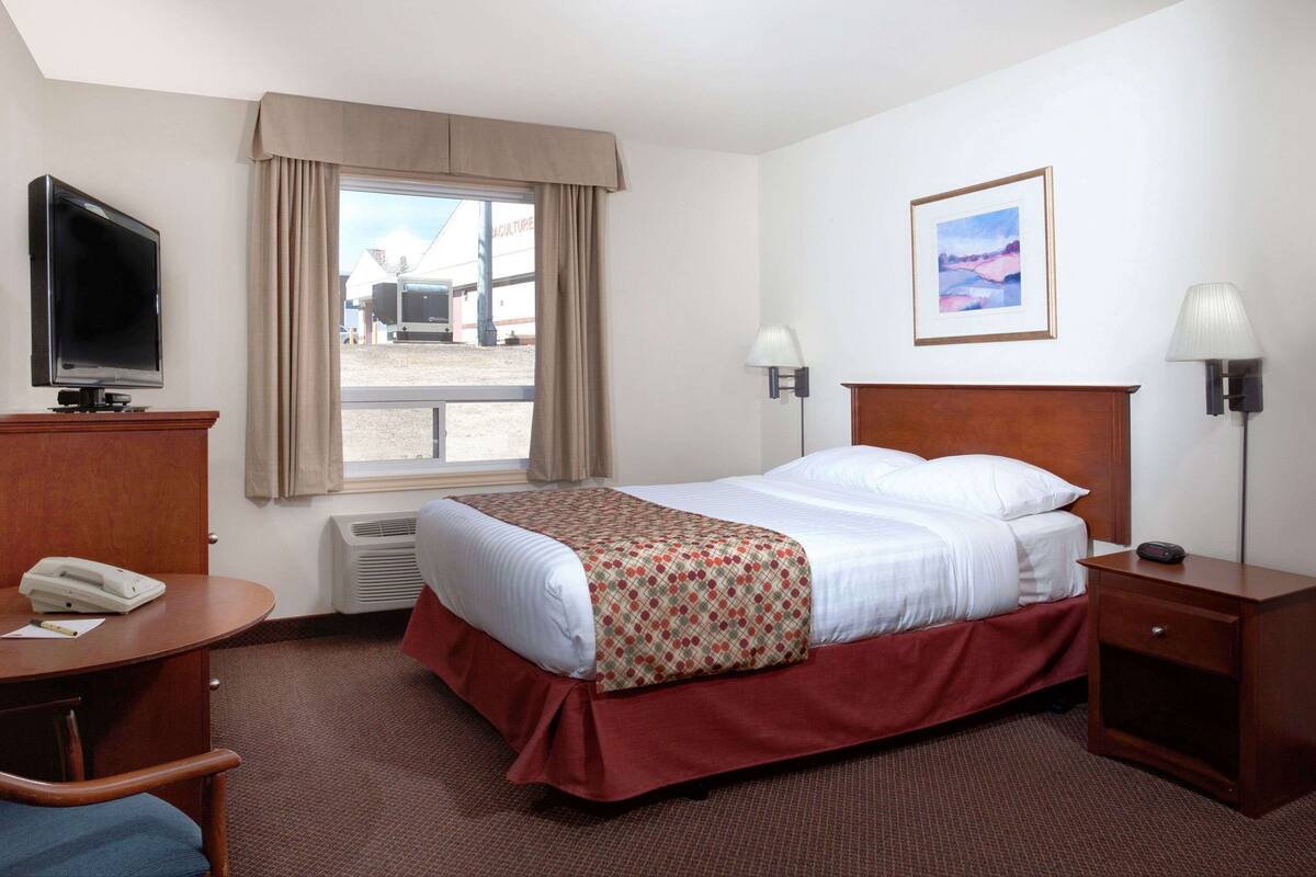 A hotel room with a bed, a desk with a telephone, a TV, and a window with curtains.