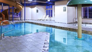 Una piscina interior con tobogán, sillas de descanso y suelo de baldosas.