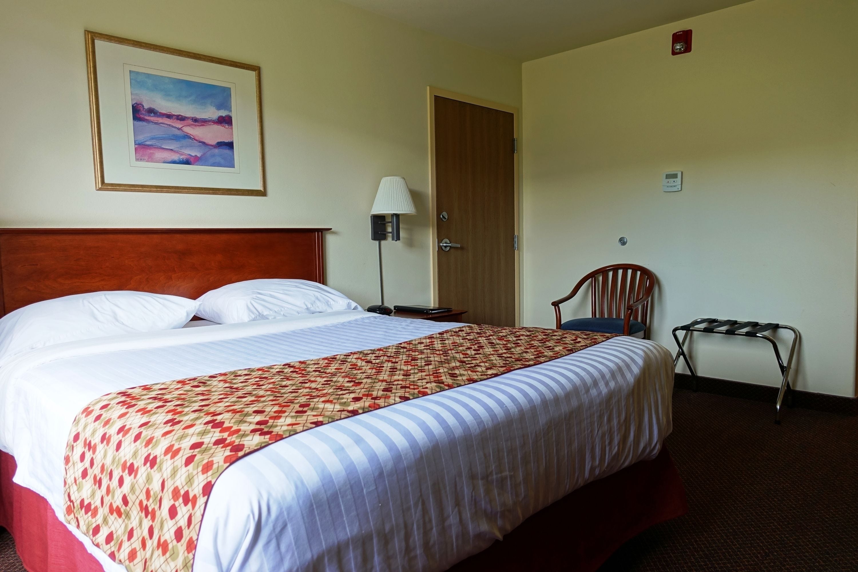Una habitación de hotel con una cama grande, una silla, una lámpara y una puerta.