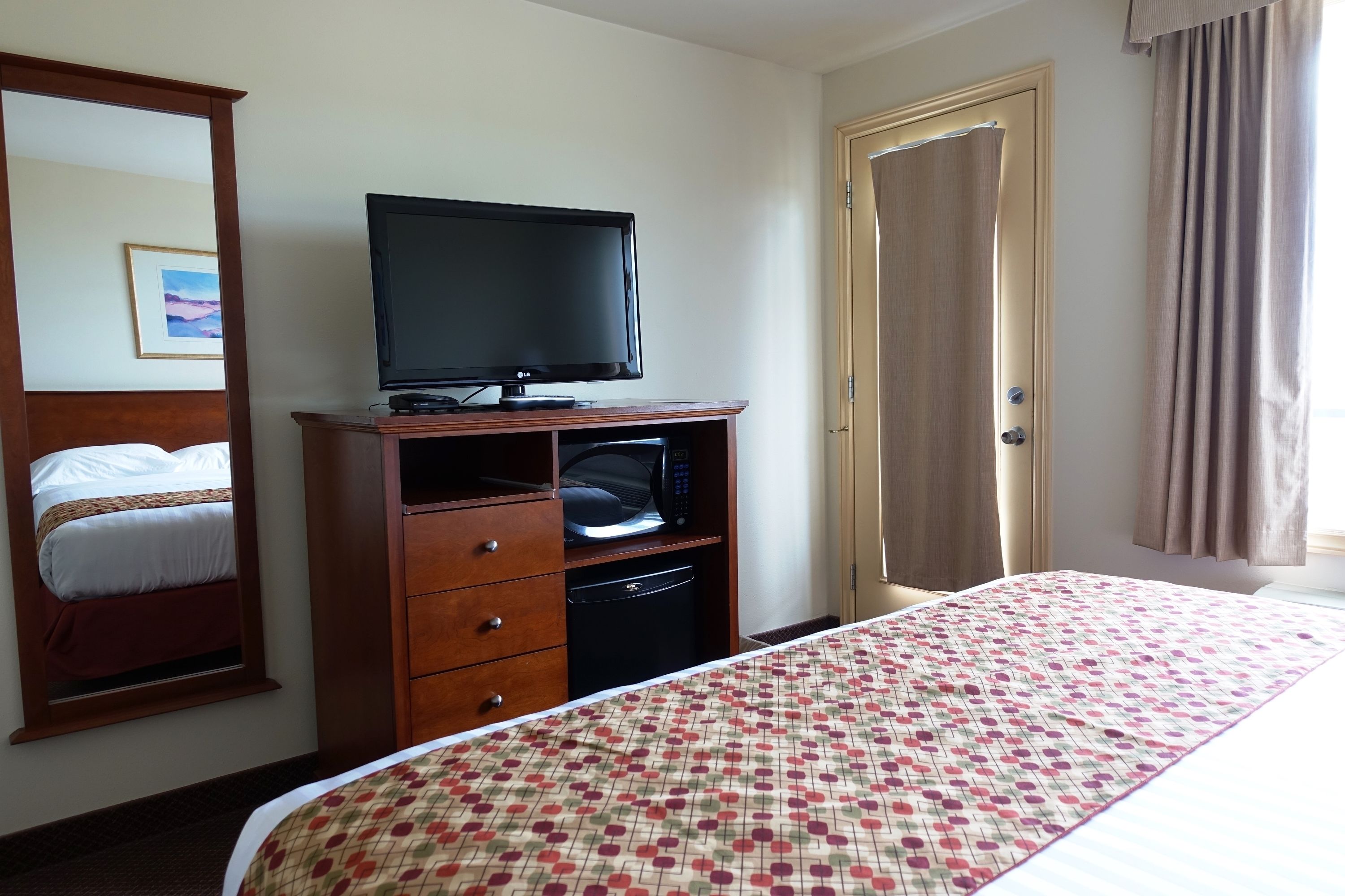 Habitación de hotel con cama, televisor sobre un mueble de madera, armario y una puerta.
