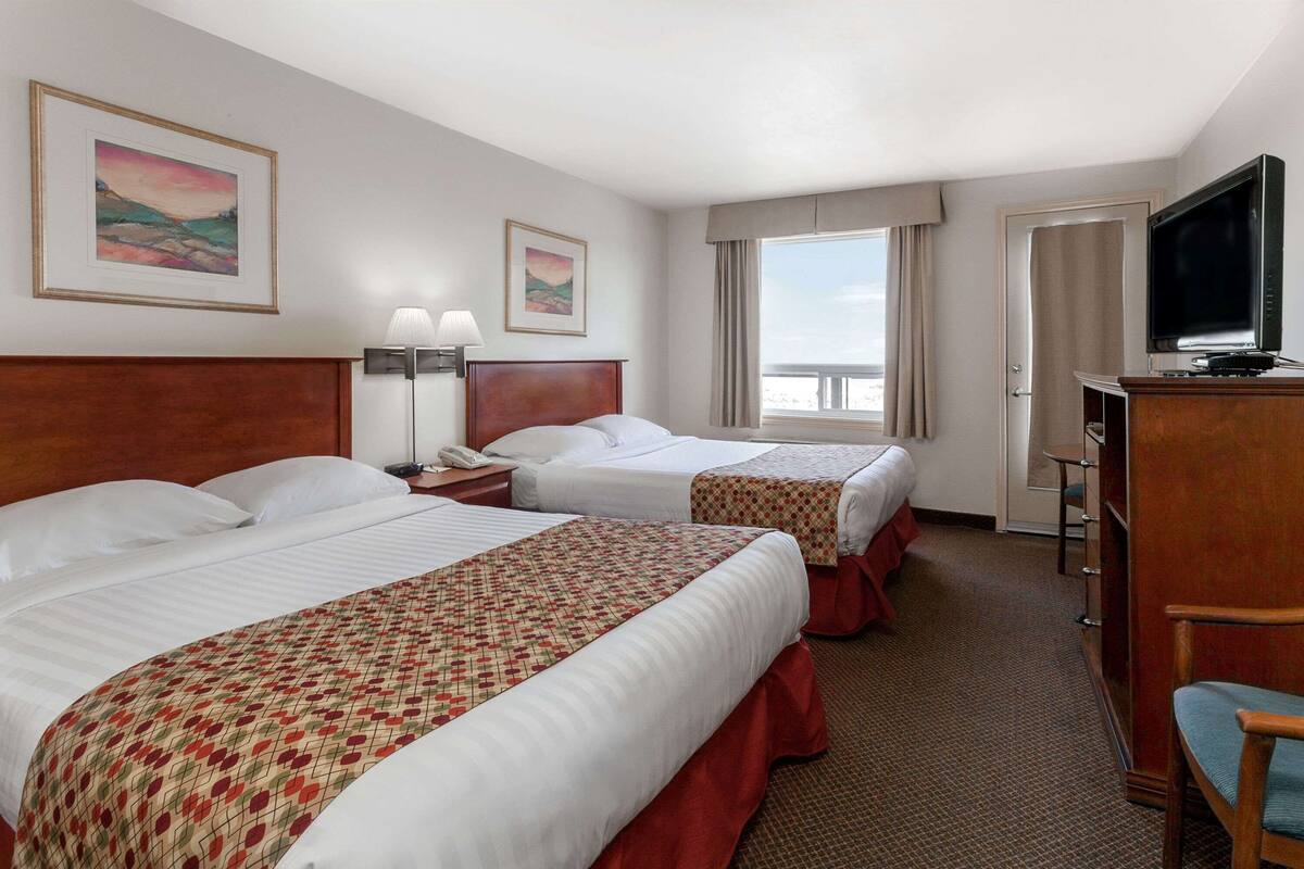 A hotel room with two beds, a desk with a television, and a window with a view.