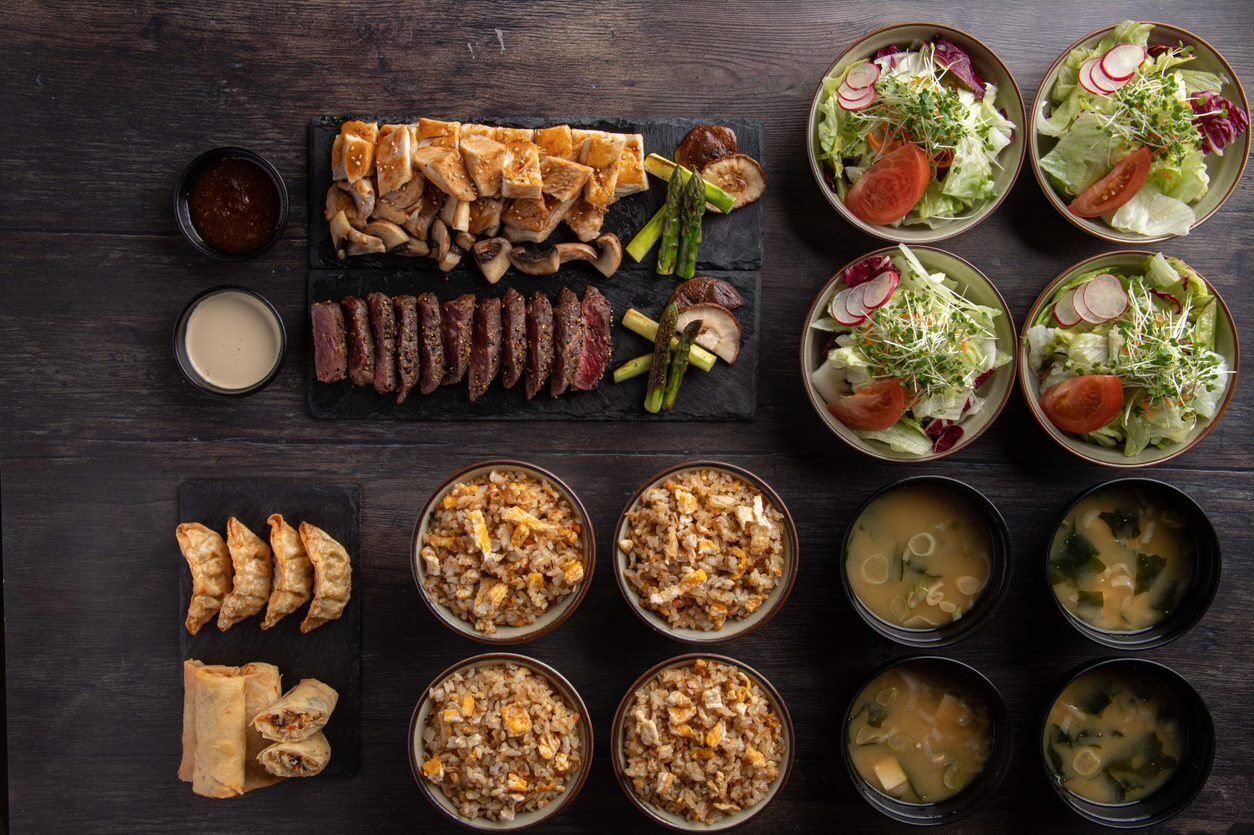 A variety of dishes including sliced meats, fried rice, and soups arranged on a dark wooden table.