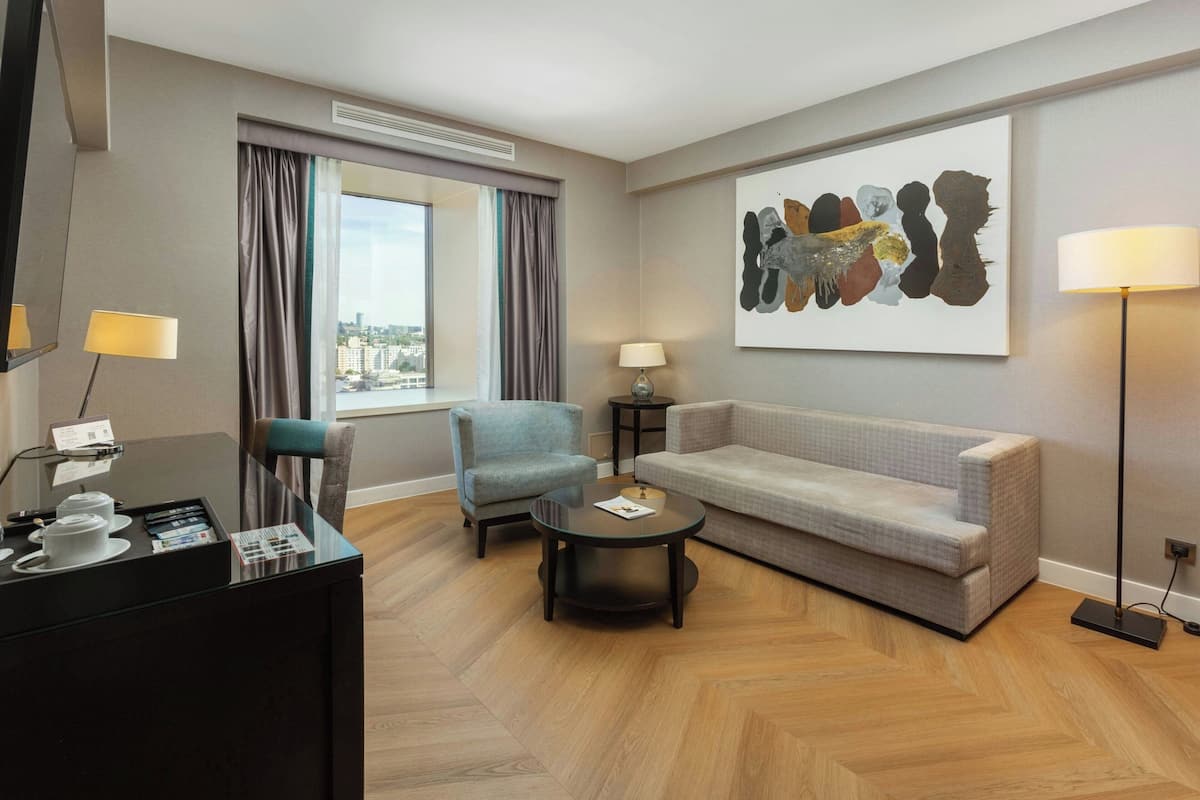Ein modernes Hotelzimmer mit Sofa, Sessel, Couchtisch und Schreibtisch mit Lampe.