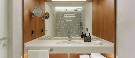 A bathroom with a wooden vanity, a sink, a mirror, and a shower.