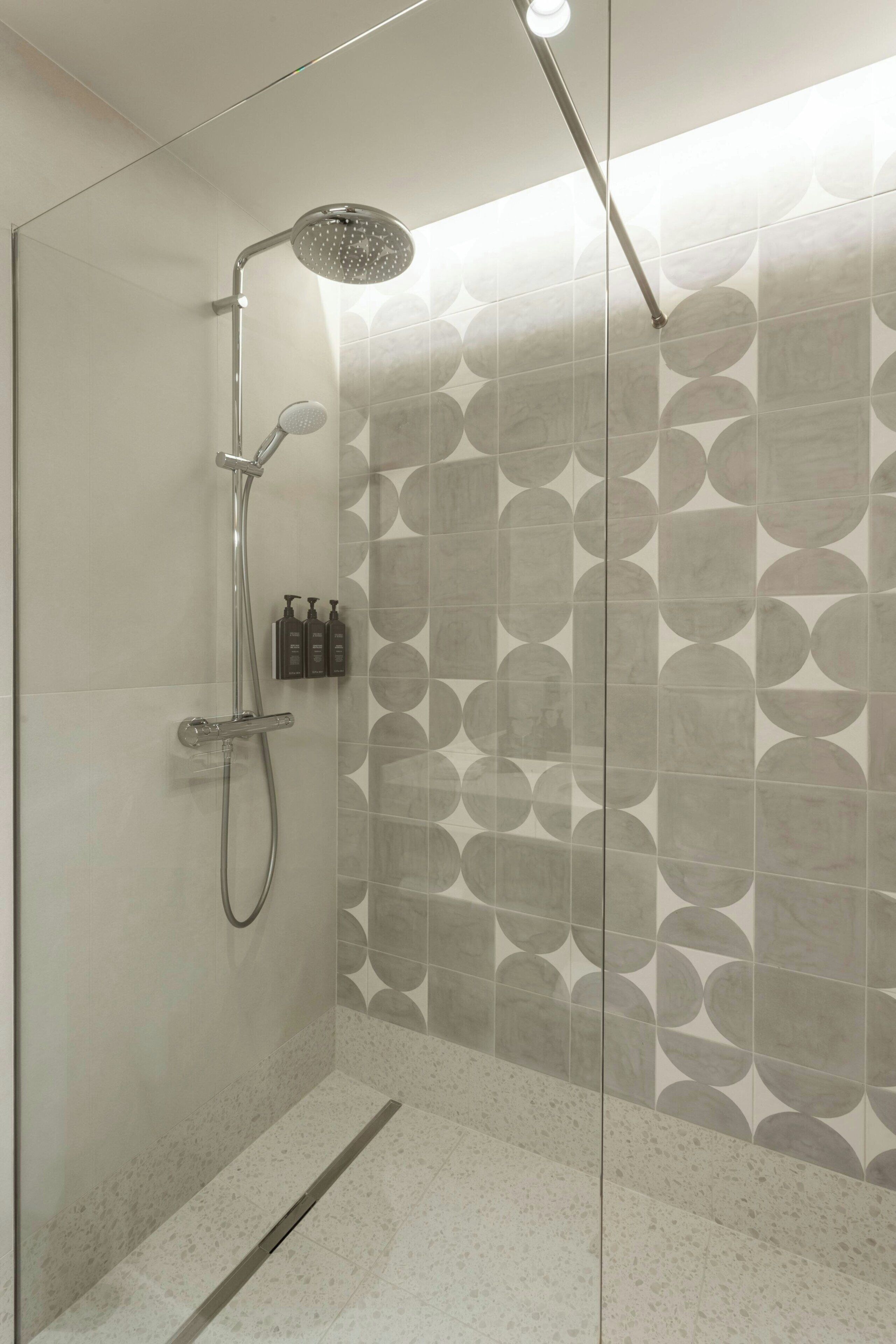 A modern shower with a handheld showerhead, a wall-mounted faucet, and a handheld showerhead.