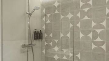 A modern shower with a handheld showerhead, a wall-mounted faucet, and a handheld showerhead.