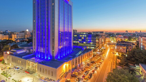 Een hoog hotel met modern design, met een opvallende verticale lichtinstallatie en een goed verlichte straat ervoor.