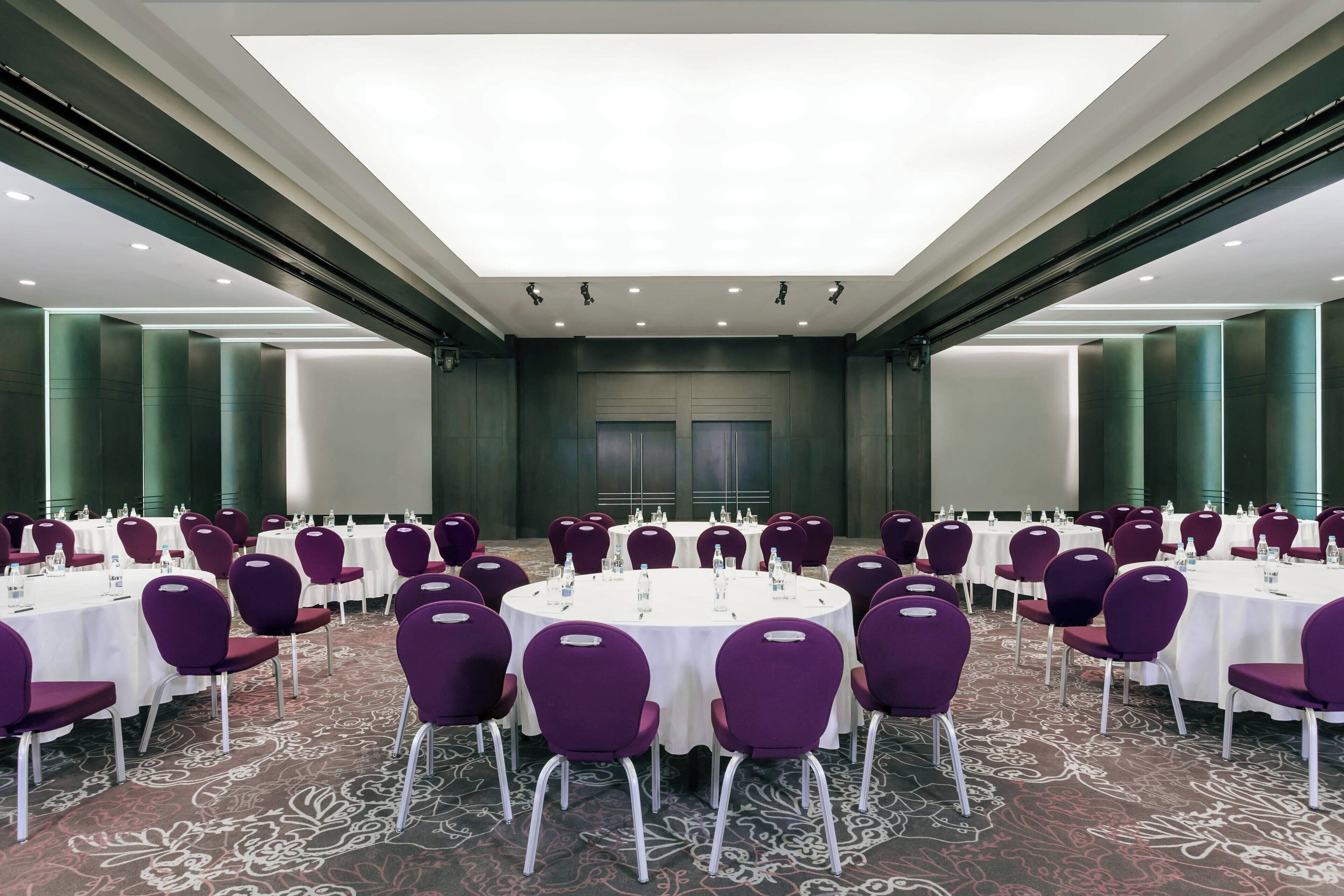 A conference room with round tables and purple chairs, equipped with water bottles and nameplates.