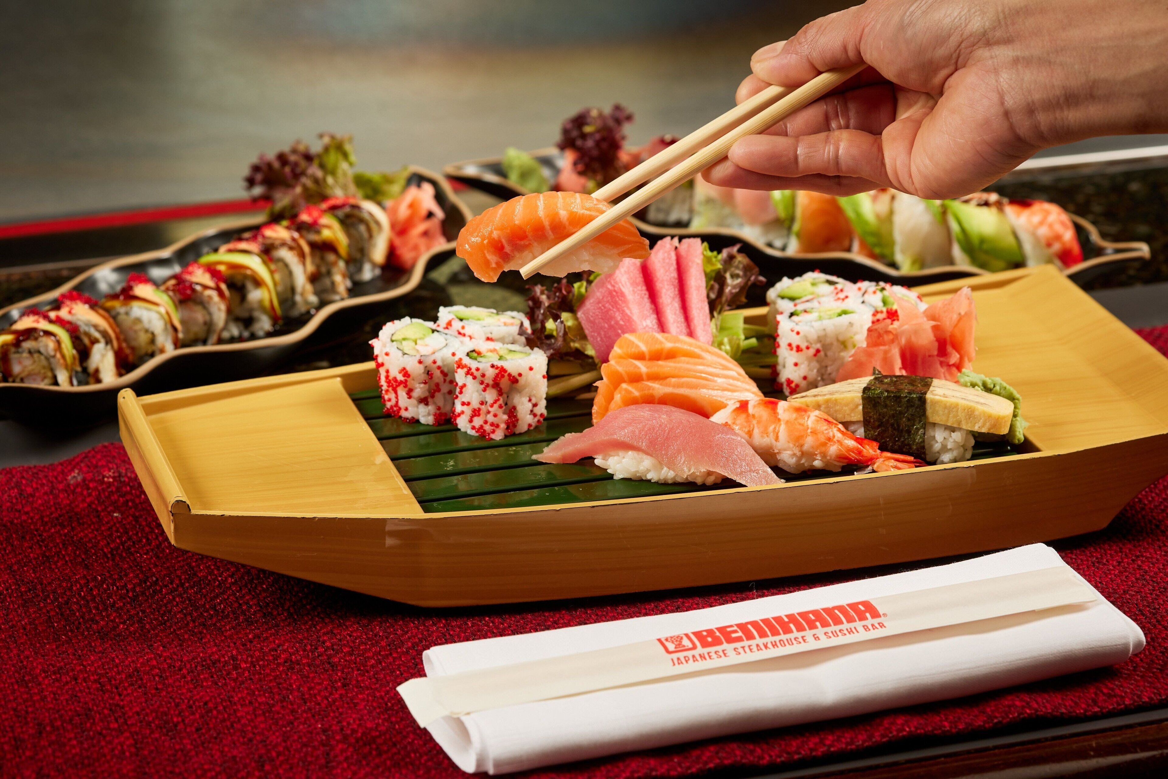 A variety of sushi on a wooden tray with chopsticks, a folded napkin, and a red textured tablecloth.